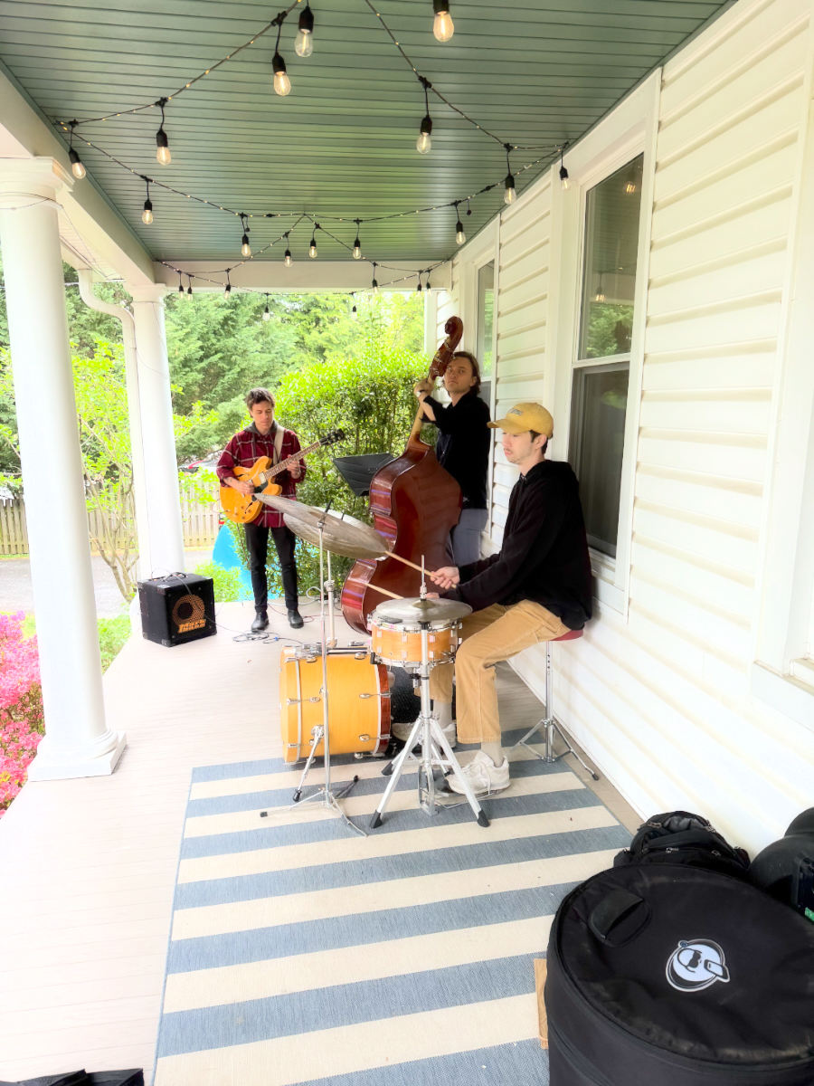 Jazz trio performing on the porch at 512 W Chesapeake Ave — guitar, upright bass, and drums under string lights